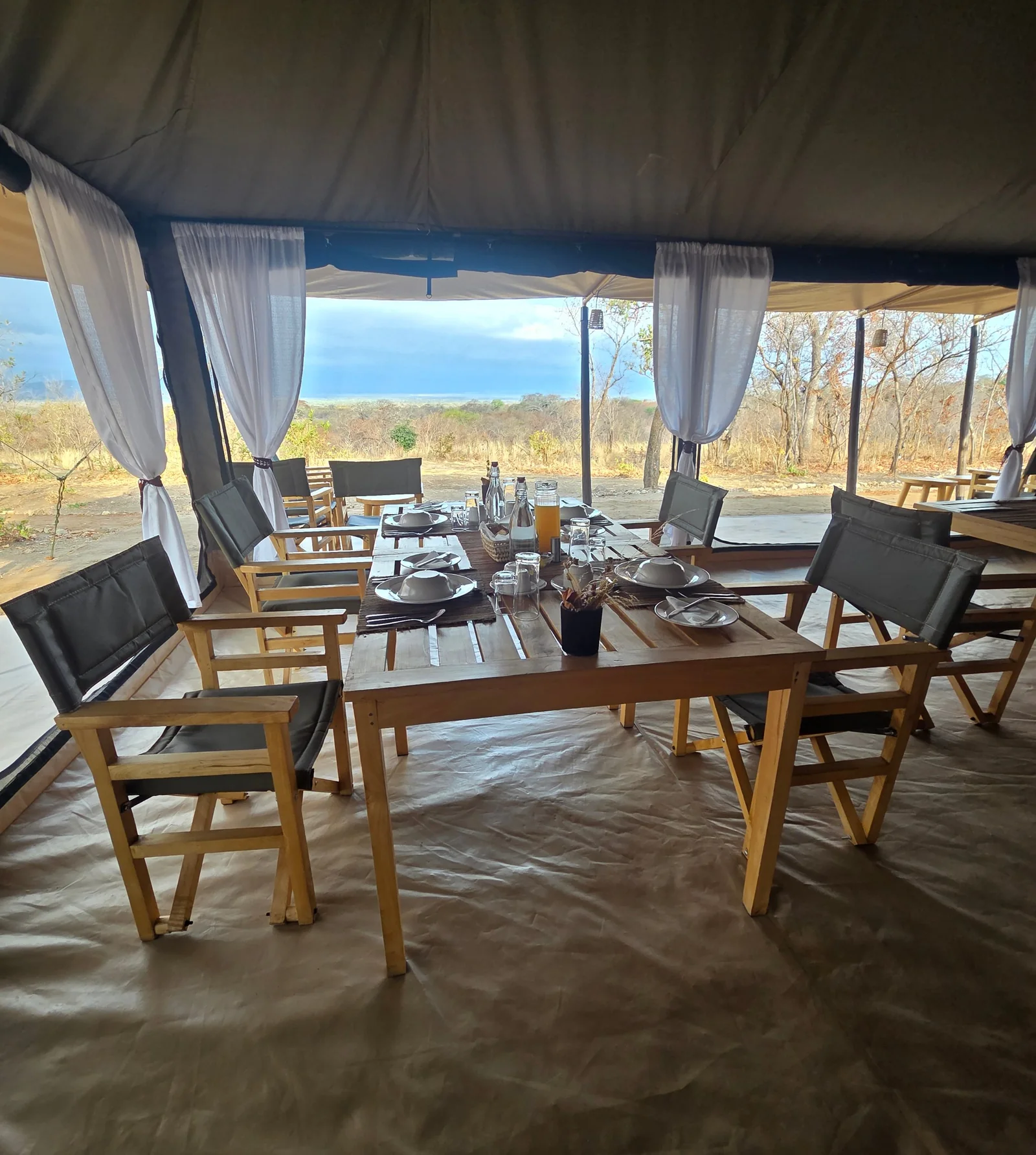 The long table in the mess tent, laid for a meal, with the bush and the lake beyond