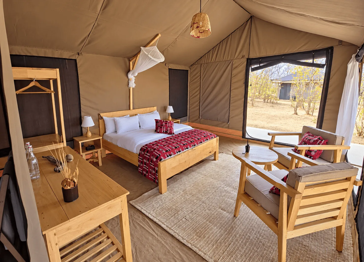 Guest tent interior with double bed, mosquito net, writing desk and two armchairs