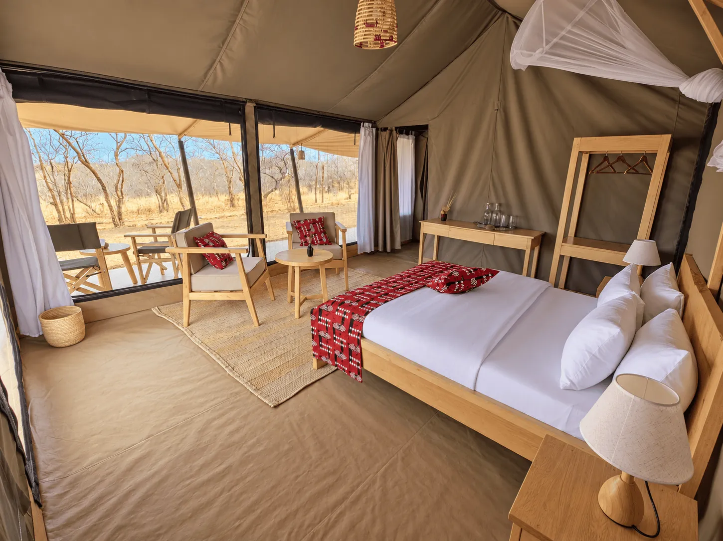 Bed and seating area inside a tent, looking out through the open front onto the veranda